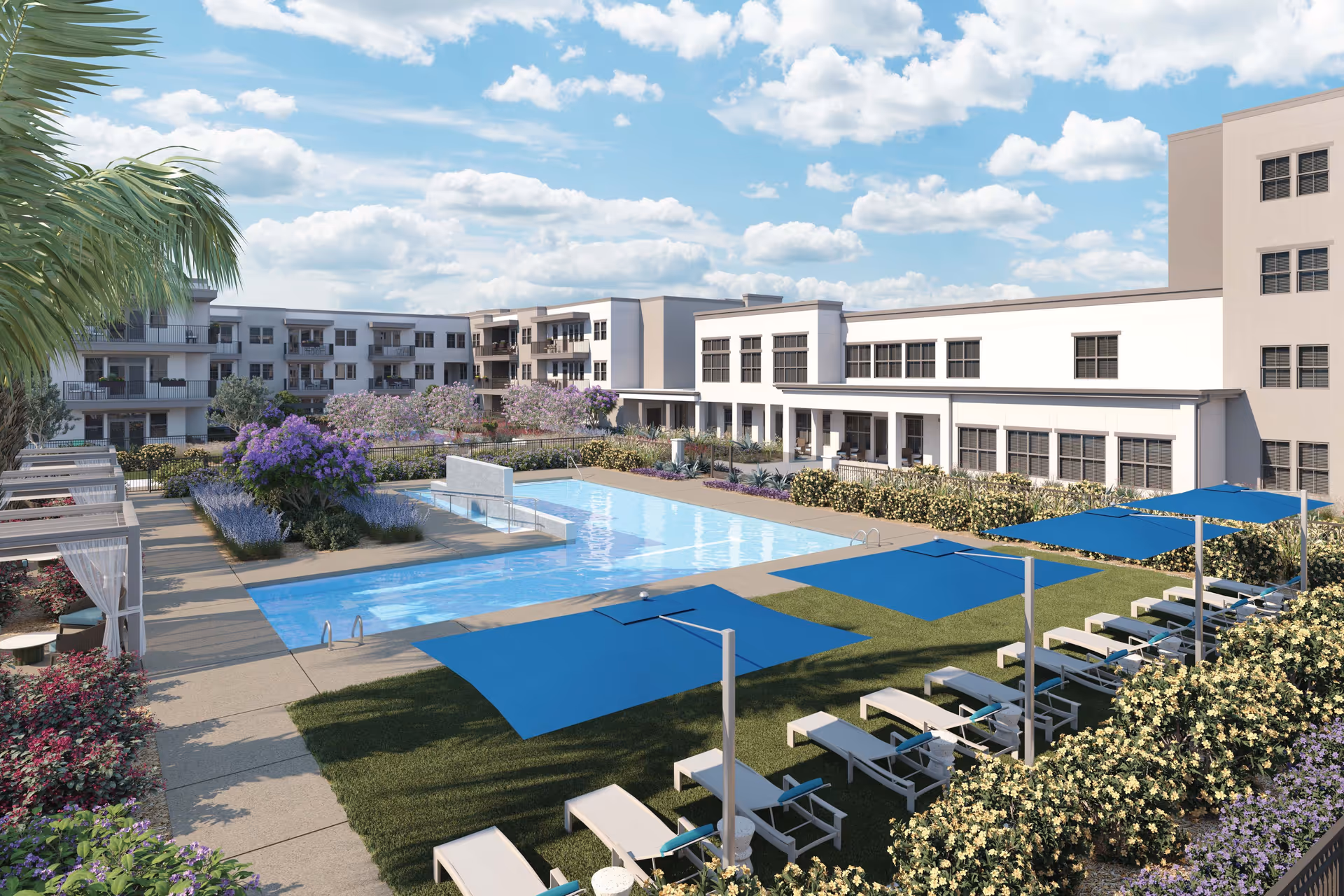 Outdoor view of a senior living facility named Mera Goodyear featuring a large swimming pool surrounded by lounge chairs with blue umbrellas, landscaped gardens with colorful flowers and shrubs, and multi-story residential buildings in the background under a partly cloudy sky.