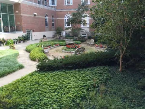 Outdoor courtyard with benches, flower beds, and a brick building in view.