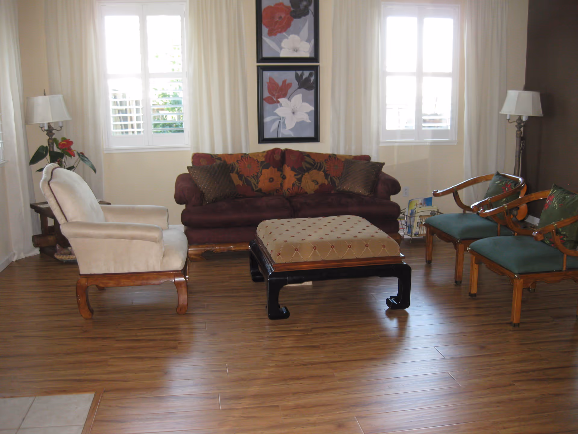 Bright living room with a sofa, armchairs, ottoman, and wooden floors in front of two windows.