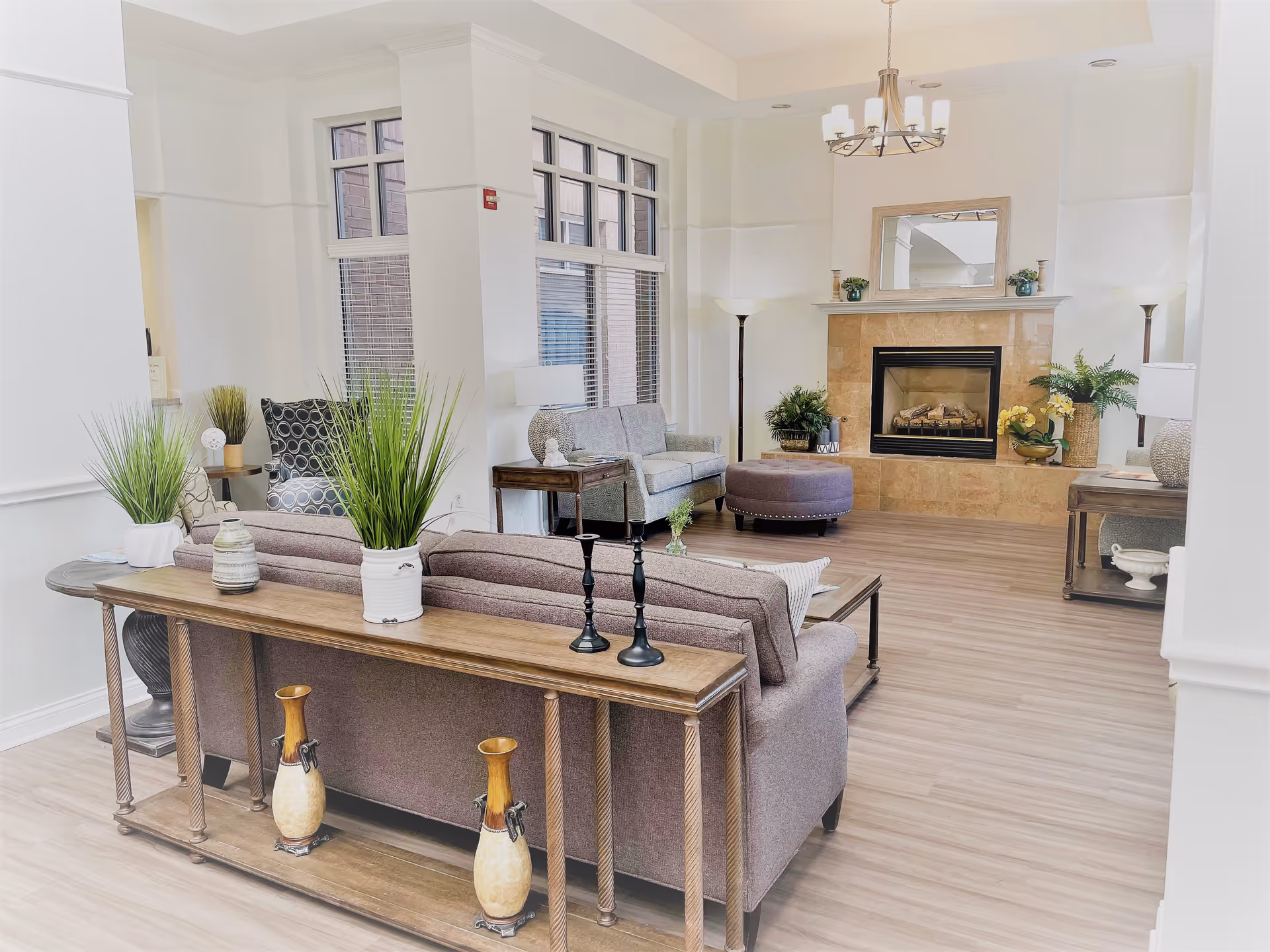 Bright living room in a senior facility with couches, a fireplace, and decorative plants.