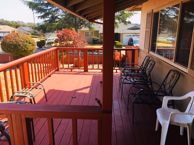Covered red wooden porch/deck with several chairs overlooking a residential street.