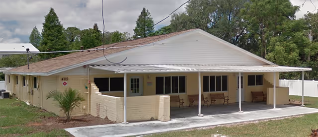 Single-story beige facility with a front covered porch and several chairs on a concrete walkway.