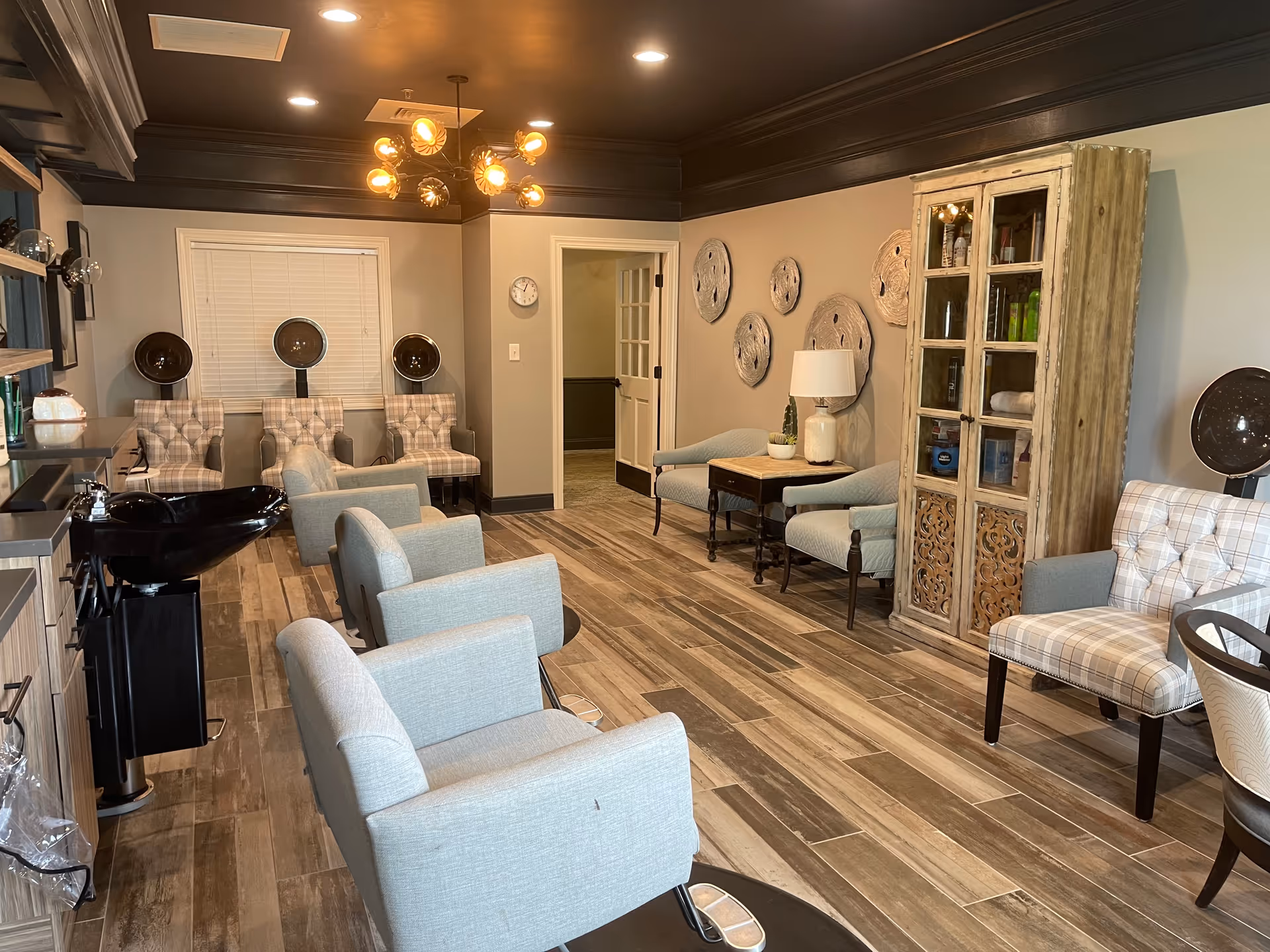Salon-style interior with multiple styling chairs, hooded hair dryers, a shampoo sink, and lounge seating.