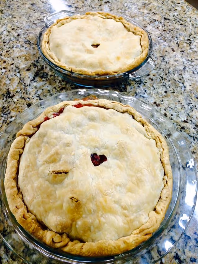Two homemade pies with golden crusts placed on a granite countertop. The pie in the foreground has a heart-shaped vent cut into the crust, while the pie in the background has a small round vent.