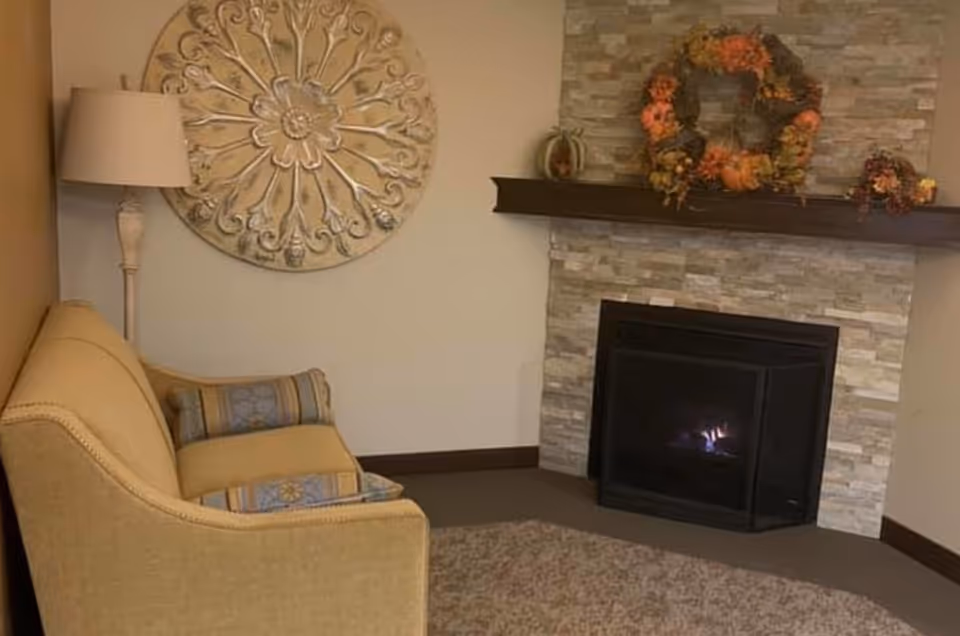 Cozy lounge with a yellow sofa, floor lamp, decorative wall art, and a lit stone fireplace topped with a wreath.