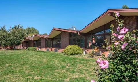 Cobblestone Court exterior with brick facade, green lawn, and pink flowering bushes.