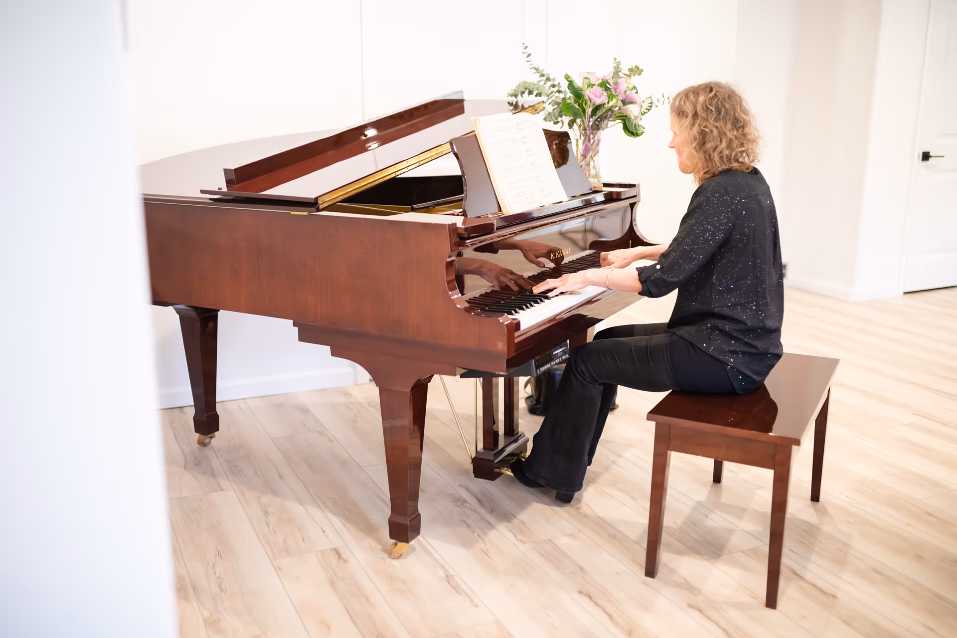 A woman plays a grand piano in a bright, airy room.