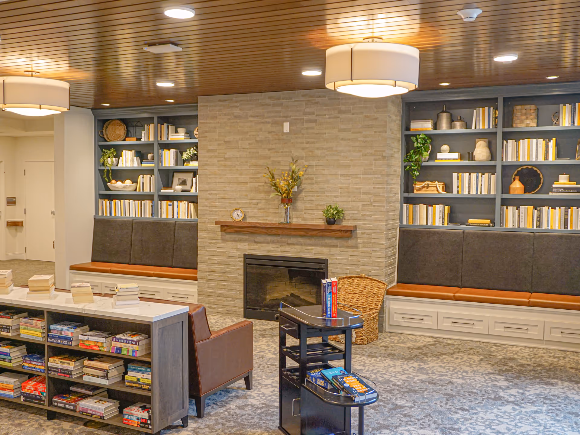 Comfortable communal lounge featuring built-in bookshelves, cushioned bench seating, a fireplace, and chairs with tables and books.