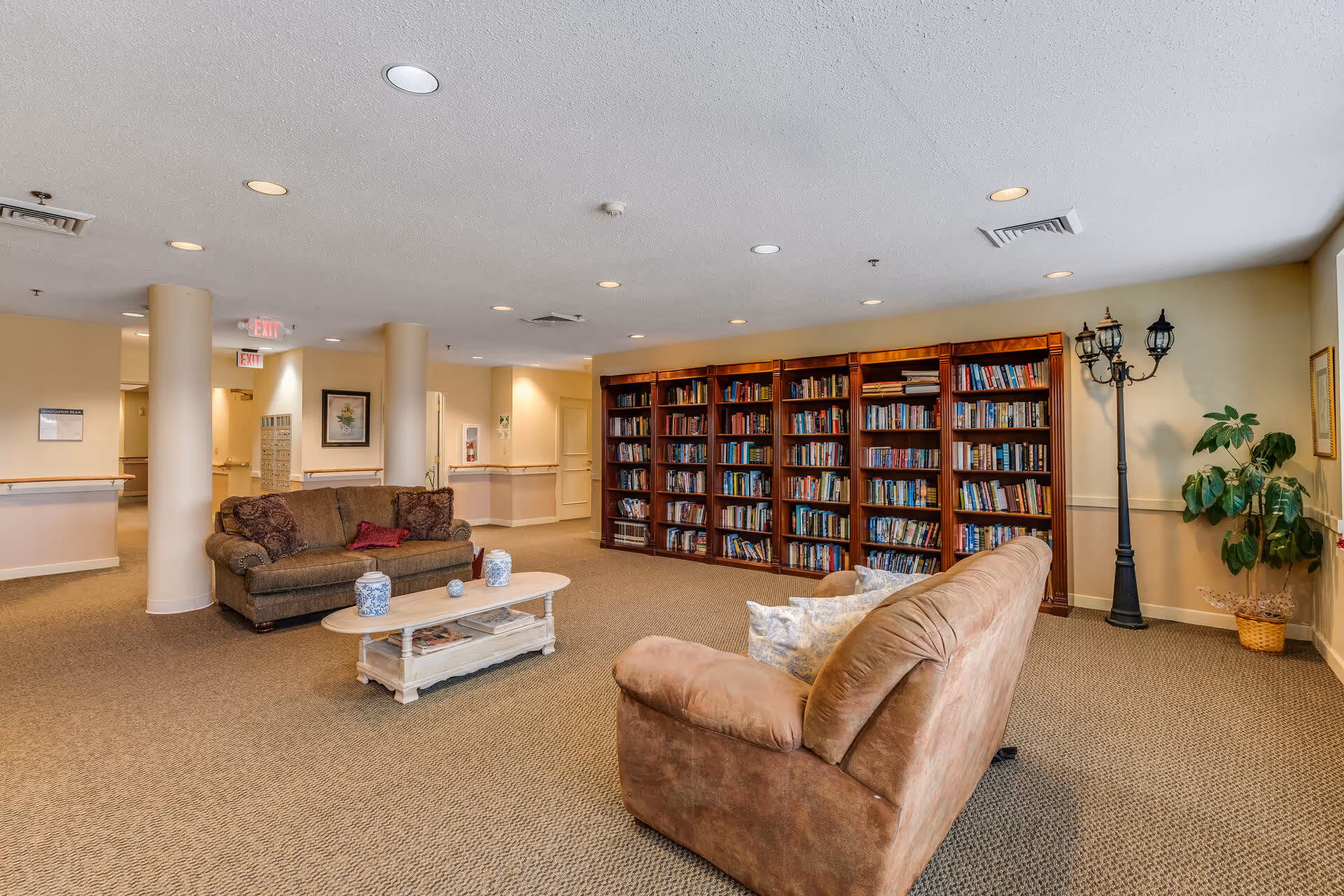 Spacious senior living common room with sofas, a coffee table, and a large bookshelf against the wall.