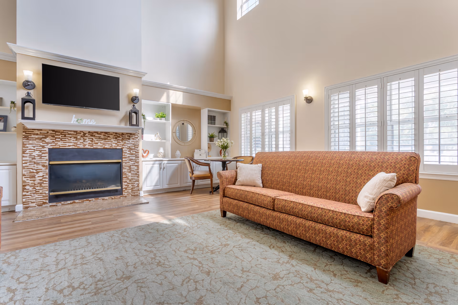Bright living room with fireplace, TV, built-in shelves, and a patterned sofa.