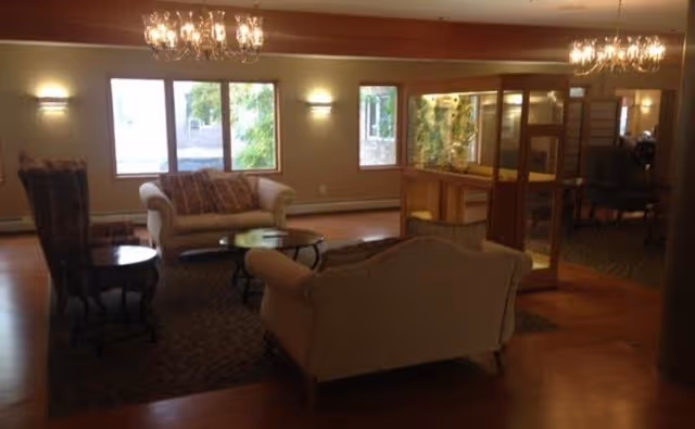 A softly lit lounge with sofas, armchairs, chandeliers, large windows, hardwood floors and a glass-enclosed fish tank divider.