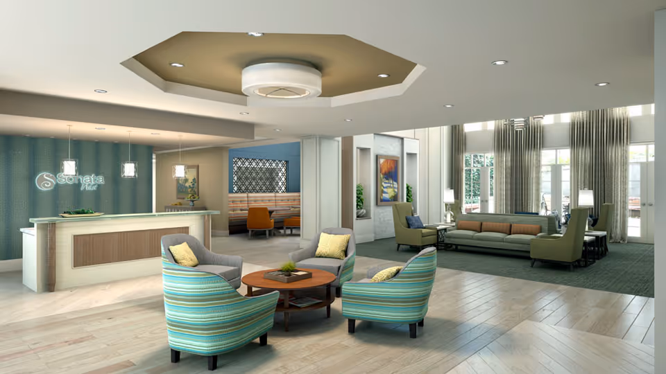 A spacious and well-lit senior living facility lobby with a reception desk on the left featuring the Sonata logo. The seating area includes four striped armchairs around a round wooden coffee table in the foreground and a sofa with armchairs near large windows with long curtains in the background. The room has light wood flooring, modern ceiling lights, and decorative artwork on the walls.