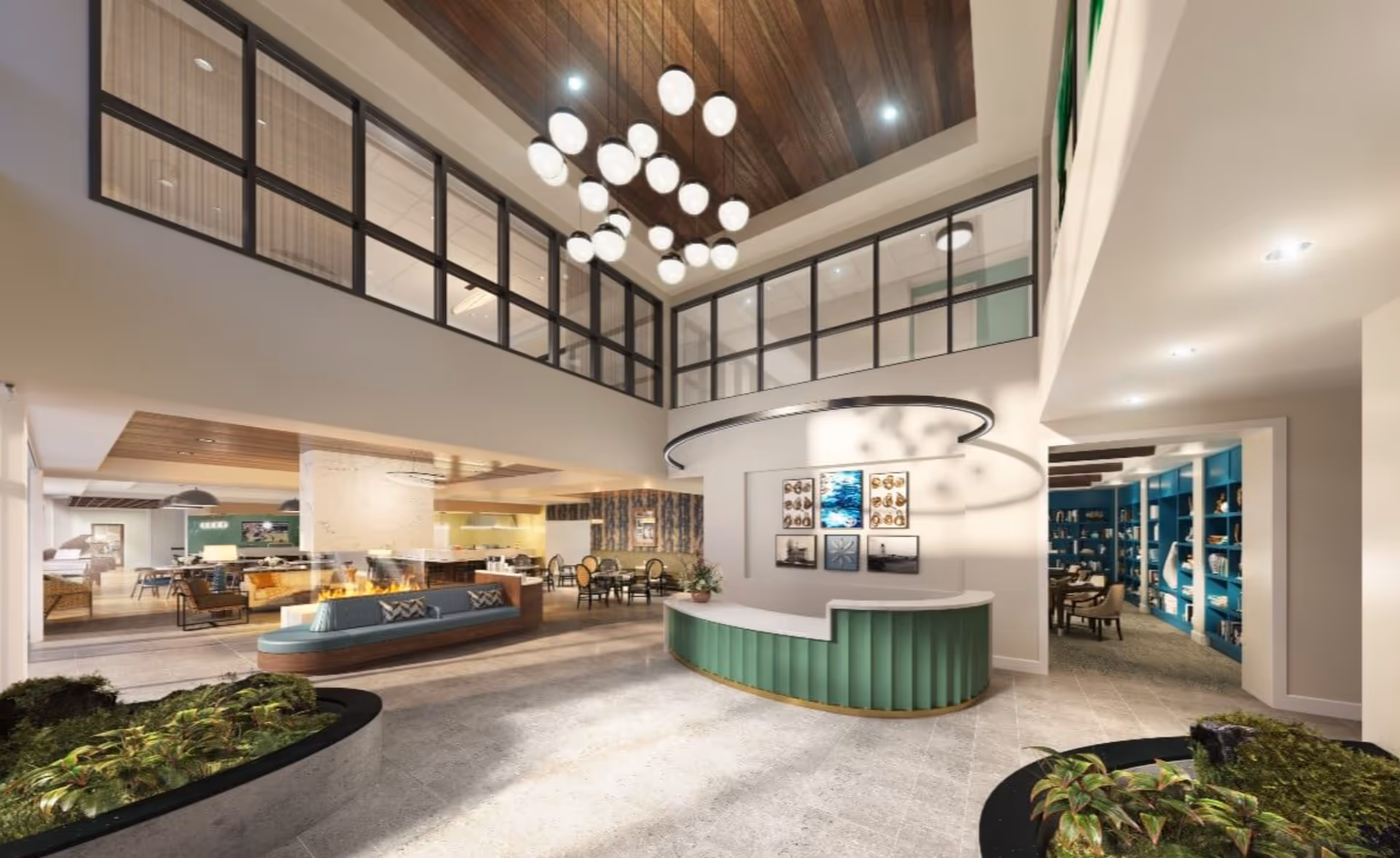 Spacious and modern interior of a senior living facility featuring a curved green reception desk with artwork on the wall behind it, a large contemporary chandelier hanging from a wooden ceiling, seating areas with tables and chairs, a fireplace, and indoor planters with greenery.