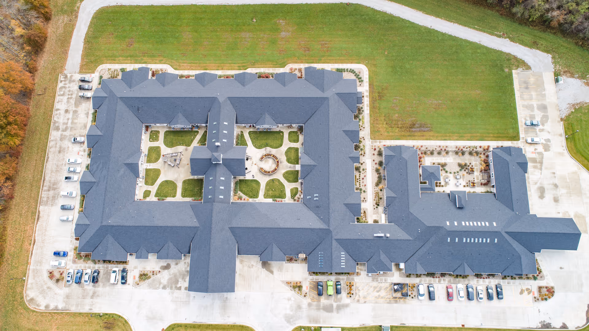 Aerial view of Villas of Holly Brook Assisted Living & Memory Care facility in Brazil, IN, showing a large building with a central courtyard, surrounding parking areas, and green lawns.