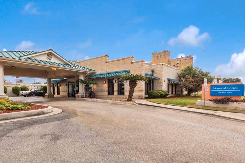 Exterior view of Memorial Medical Nursing Center showing a single-story building with a covered entrance driveway, landscaped greenery, and a sign with the facility's name on the right side.