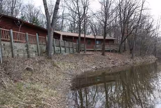 Red wooden building along a pond with a fence and leafless trees.