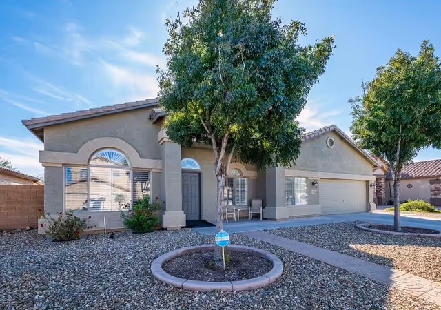 Single-story adult care facility exterior with arched windows, front door, and surrounding trees.