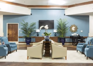 Communal lounge with sofas and armchairs arranged around a central TV, potted plants, and decorative accents.