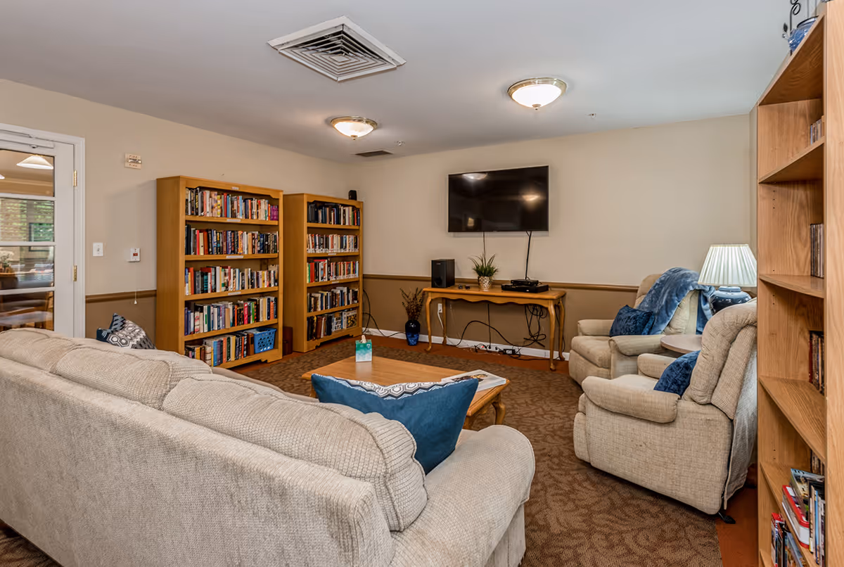 Cozy common room with sofas, armchairs, bookshelves and a wall-mounted TV.