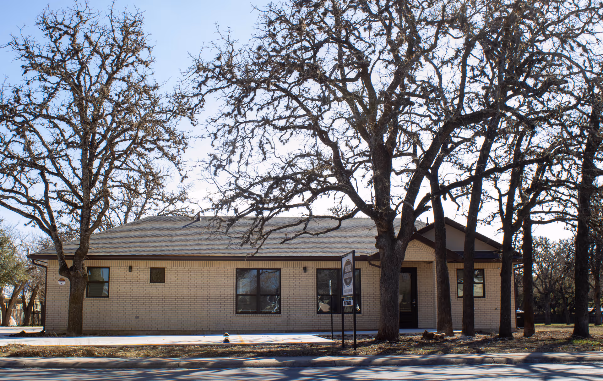 Single-story brick assisted living building with a front entrance and sign, framed by leafless trees.