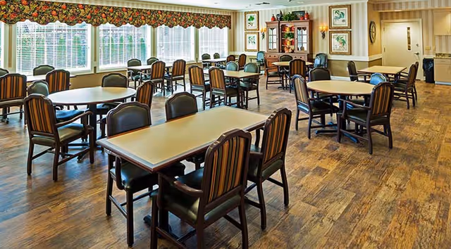 Bright dining room with round and rectangular tables and striped upholstered chairs on wood flooring beneath large windows.