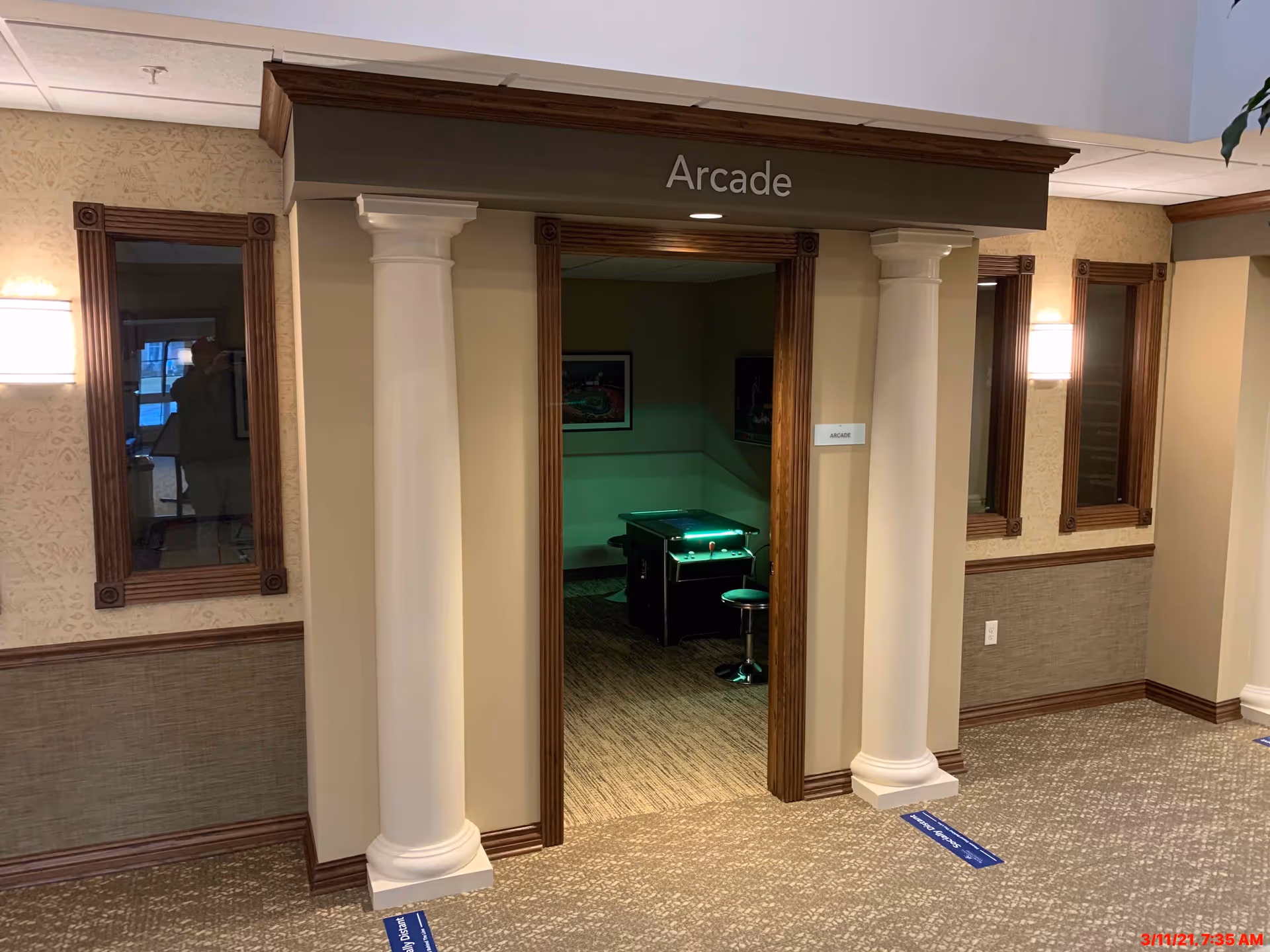 A hallway entrance framed by decorative columns leads into an arcade room with an illuminated arcade machine visible inside.