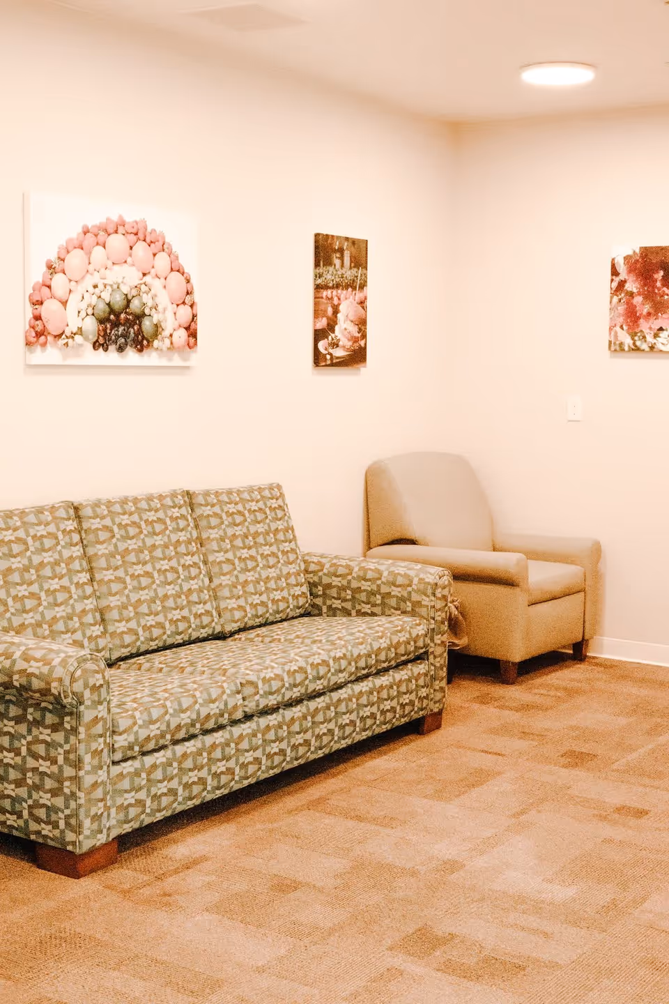A sitting area with a patterned sofa and a beige armchair against a wall adorned with framed artwork.