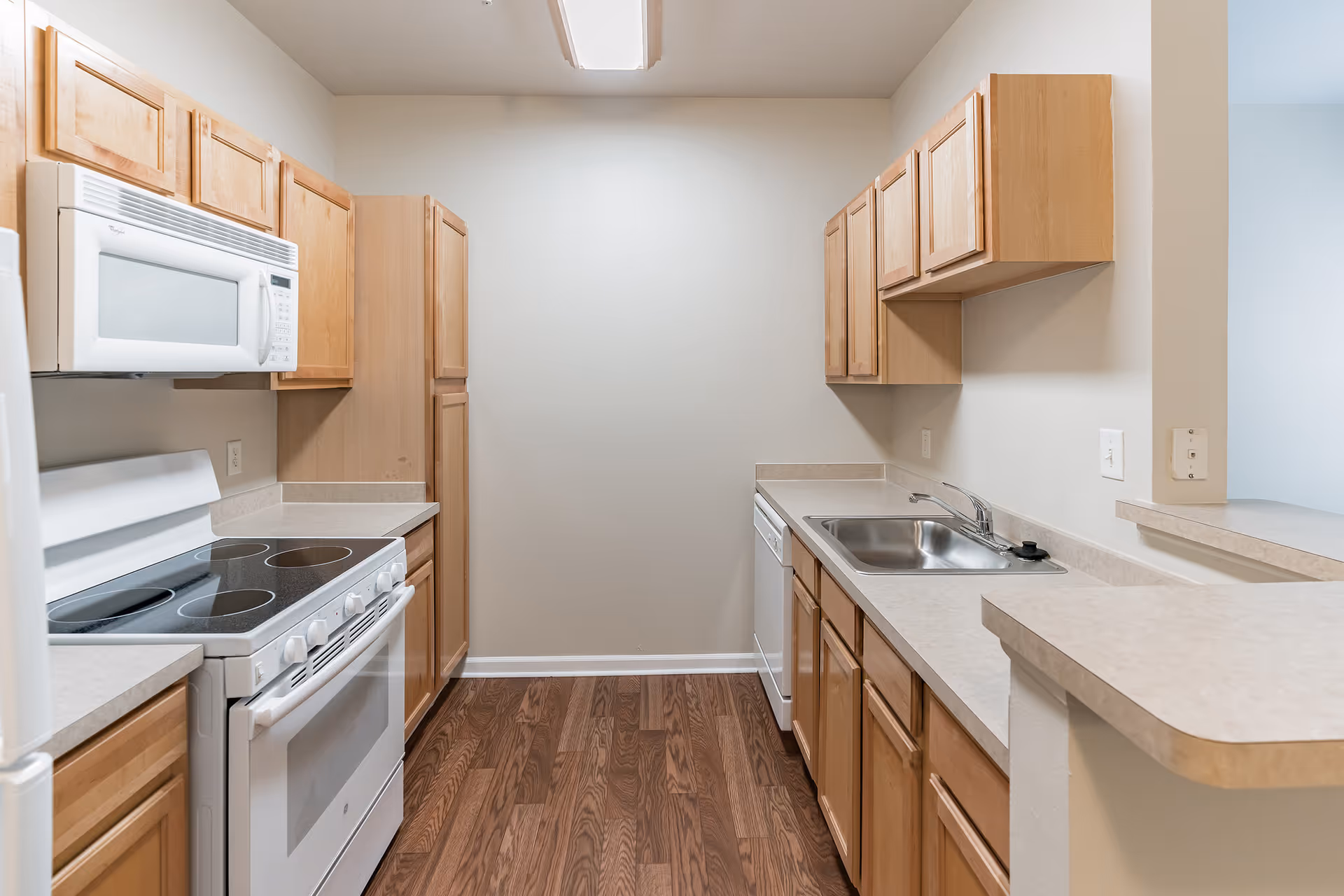 Galley kitchen with light wood cabinets, white stove and microwave, dishwasher, sink, and laminate countertops.