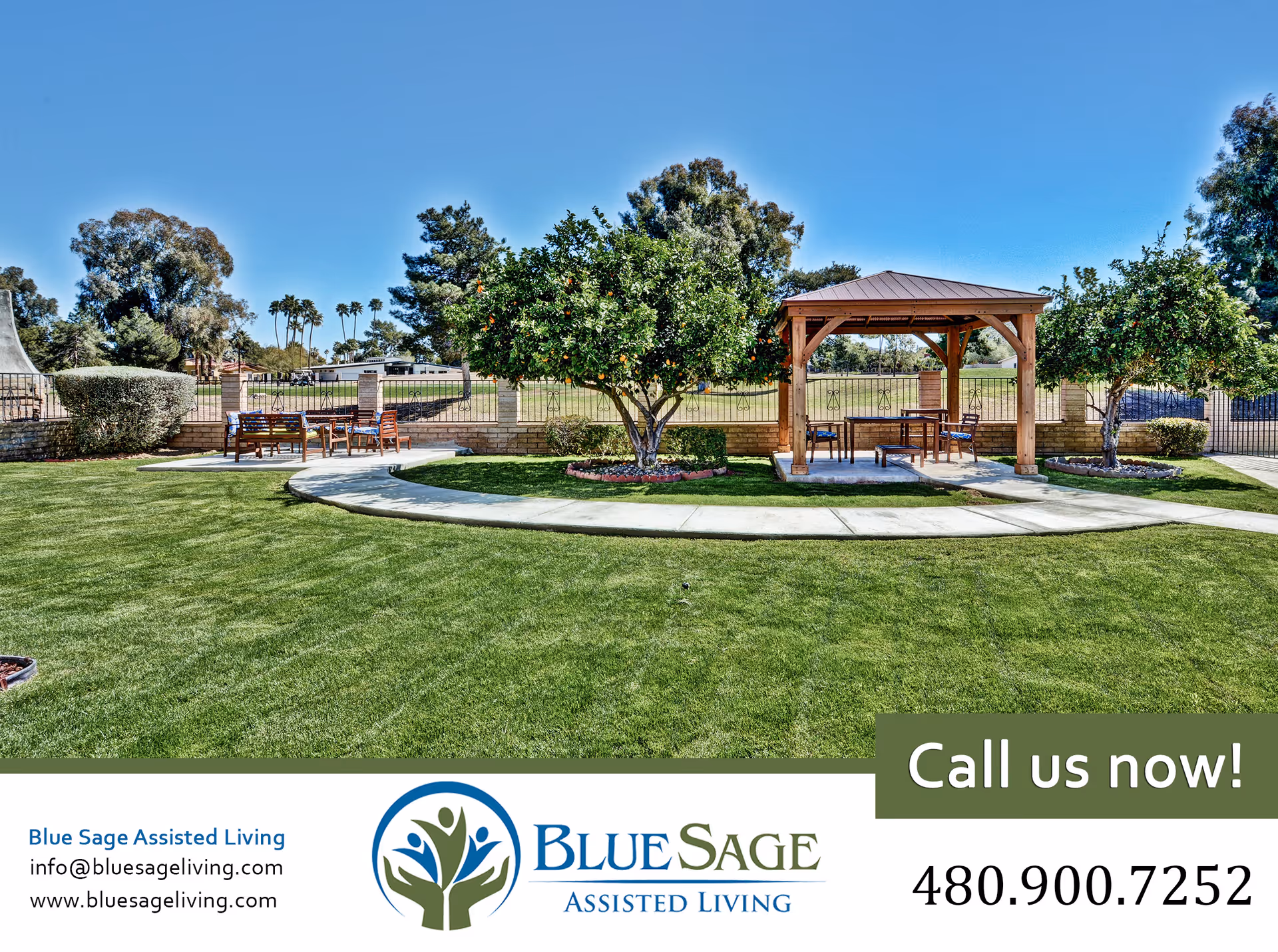 Outdoor garden area at Blue Sage Assisted Living featuring a well-maintained lawn, a curved concrete walkway, several orange trees, wooden benches and tables, and a wooden gazebo under a clear blue sky.
