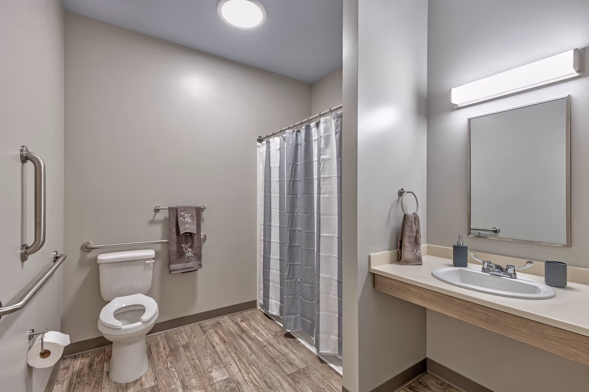 Accessible bathroom with a toilet and grab bars, a shower with curtain, and a sink with mirror and vanity.