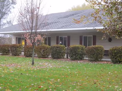 Exterior of a single-story assisted living facility with trimmed hedges and autumn leaves.