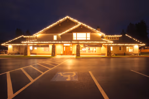 Night view of the lodge's front exterior decorated with string lights, with a parking lot and a marked handicap space in the foreground.