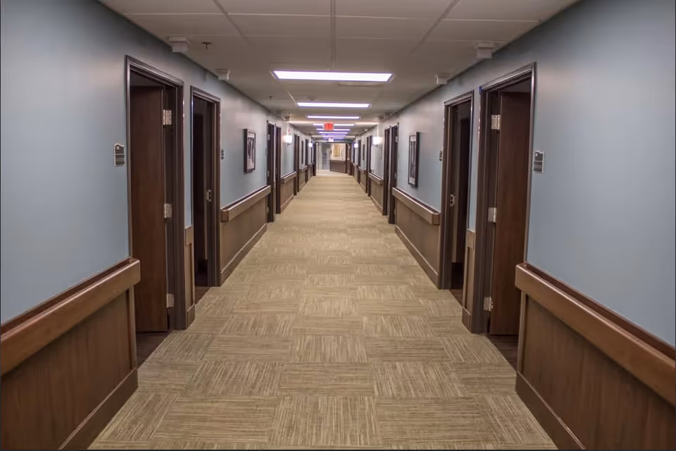 Long carpeted interior hallway with doors and wooden handrails on both sides.