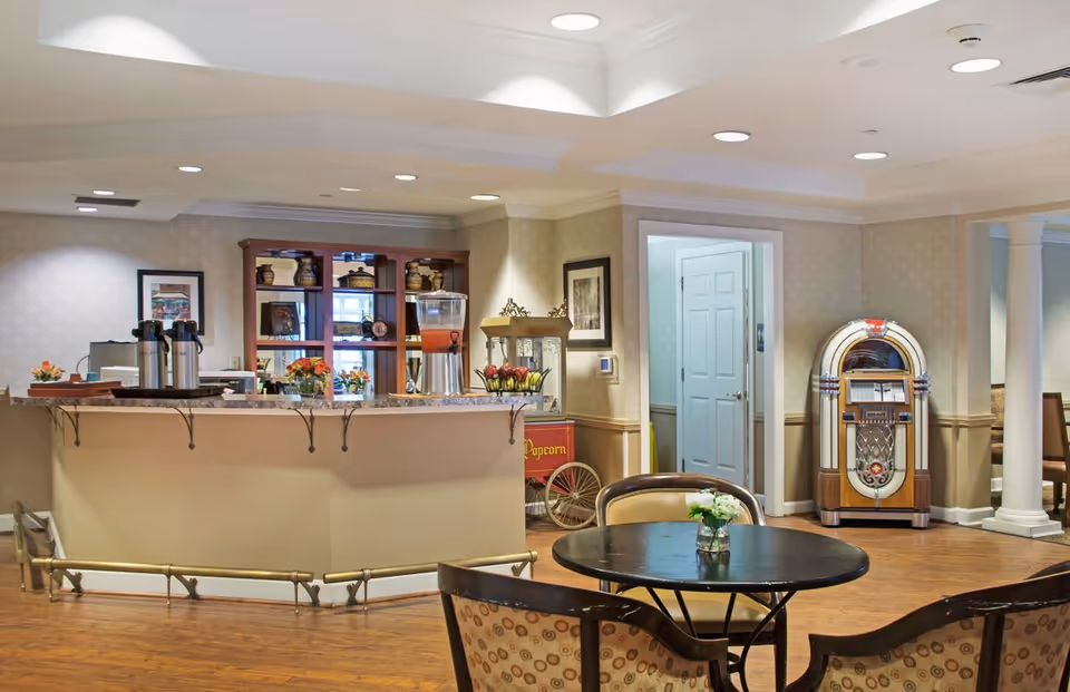 Bright communal seating and snack bar area with round tables, a service counter, a popcorn cart, and a vintage jukebox.