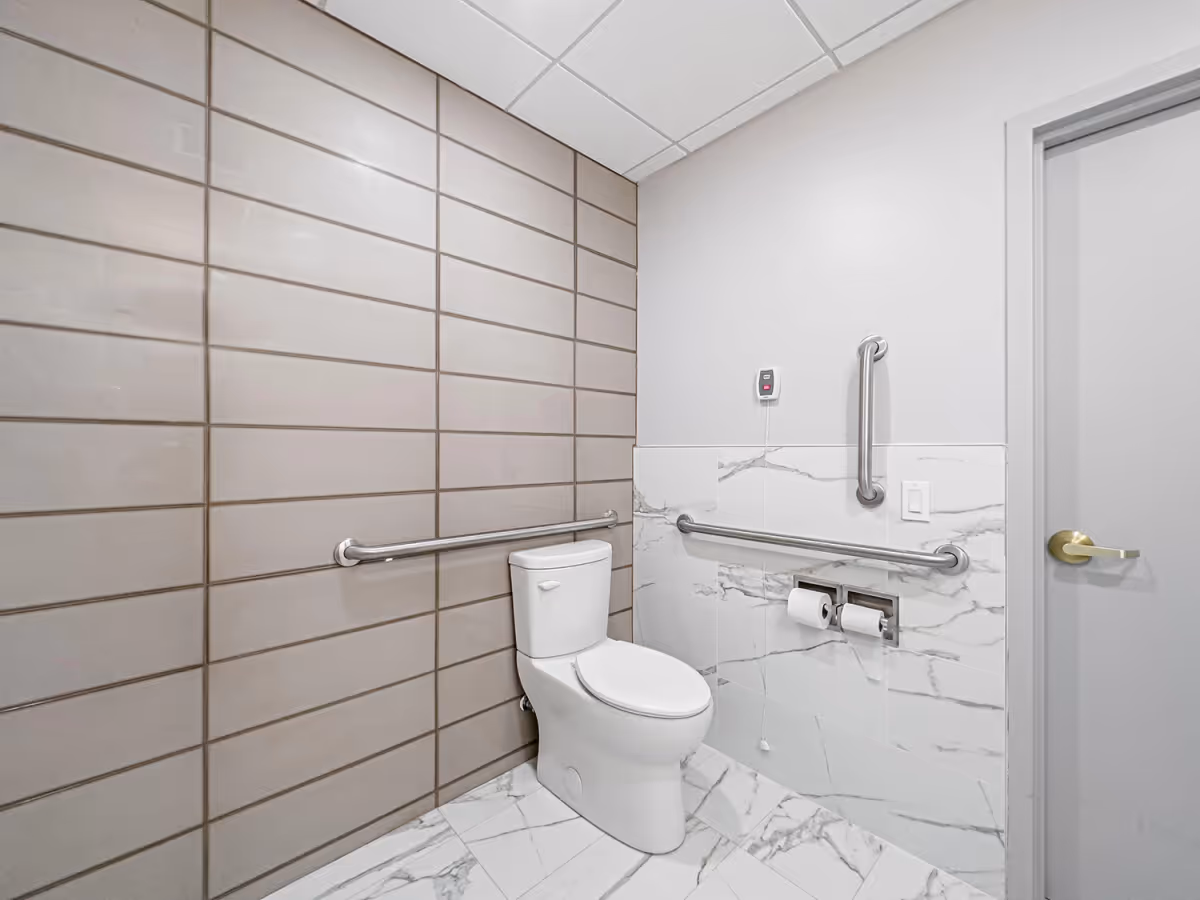 Accessible bathroom with a toilet, grab bars, and tiled walls.