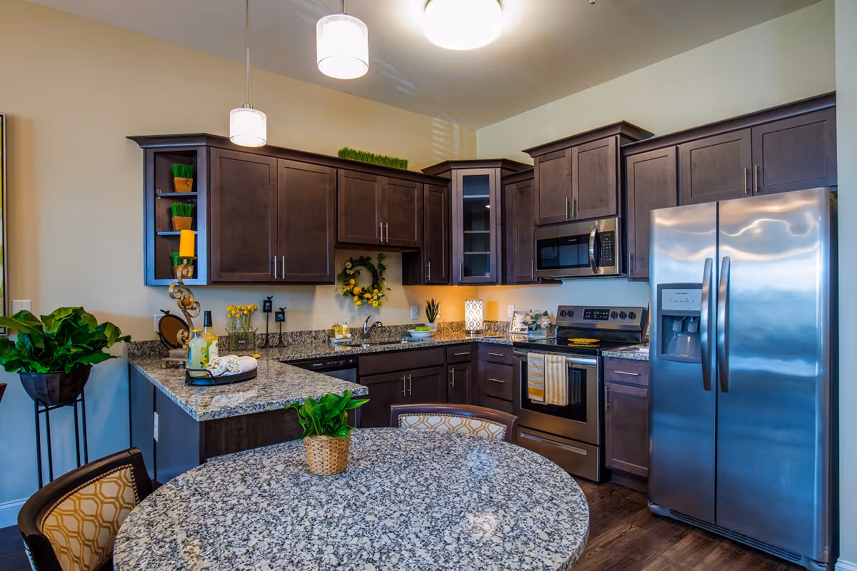 Modern kitchen with dark wood cabinets, stainless steel appliances, granite countertops and a round dining table with plants.