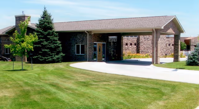 Brick single-story building with a covered entrance/porte-cochère and a well-manicured lawn in front.