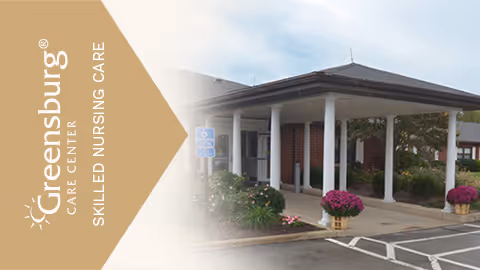 Entrance of Greensburg Care Center skilled nursing facility with a covered drop-off area, white columns, potted flowers, and a parking lot with handicapped parking spaces.