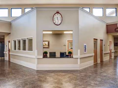 Reception lobby inside a senior living facility with a central desk and clock.