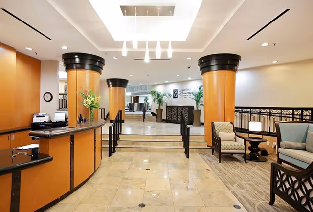 Spacious senior living lobby with a curved reception desk, large decorative columns, seating area, and overhead lighting.
