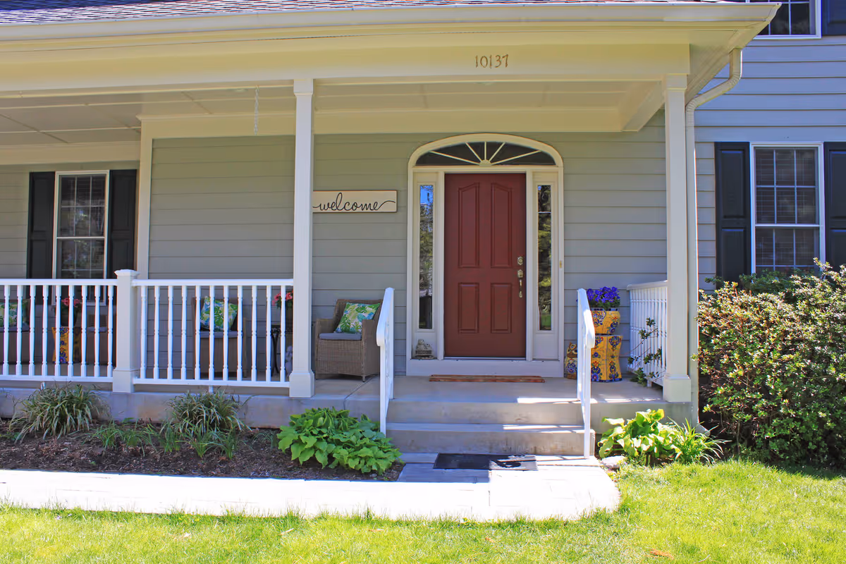 Front entrance of a senior living facility with a red door and porch seating.