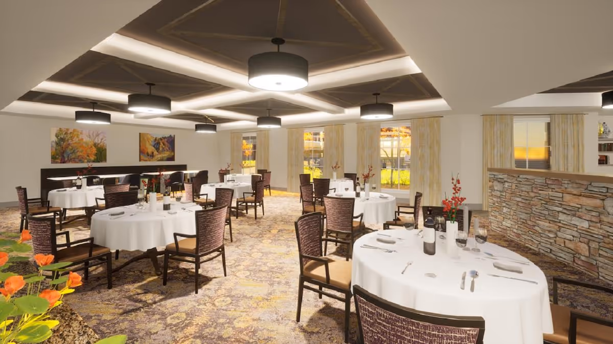 A spacious dining room with round tables covered in white tablecloths, set with plates, glasses, and silverware. The room features multiple chairs around each table, large windows with light-colored curtains, colorful paintings on the walls, and modern ceiling lights. There is a stone accent wall on one side and floral arrangements on the tables.