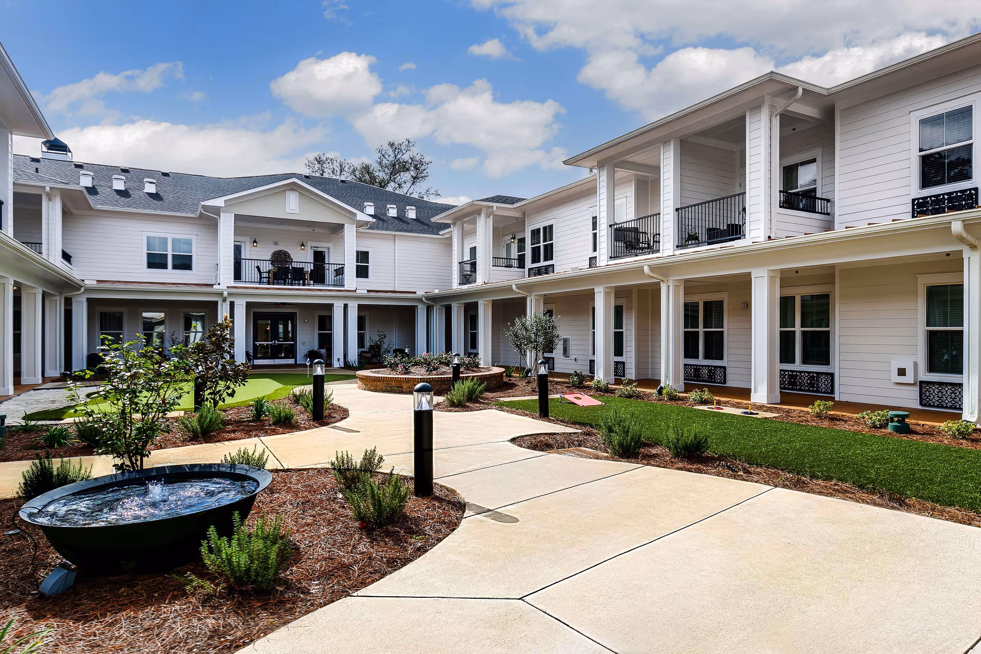 Courtyard of a two-story senior living facility with covered walkways, balconies, landscaped paths and a small fountain.