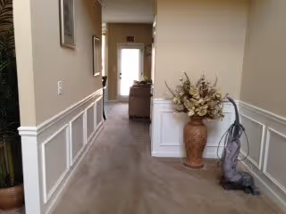 Carpeted interior hallway with wainscoting, a console table at the end, decorative vase, and a vacuum cleaner against the wall.