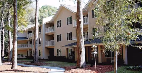 Exterior view of a beige multi-story senior living building with trees and walkway.