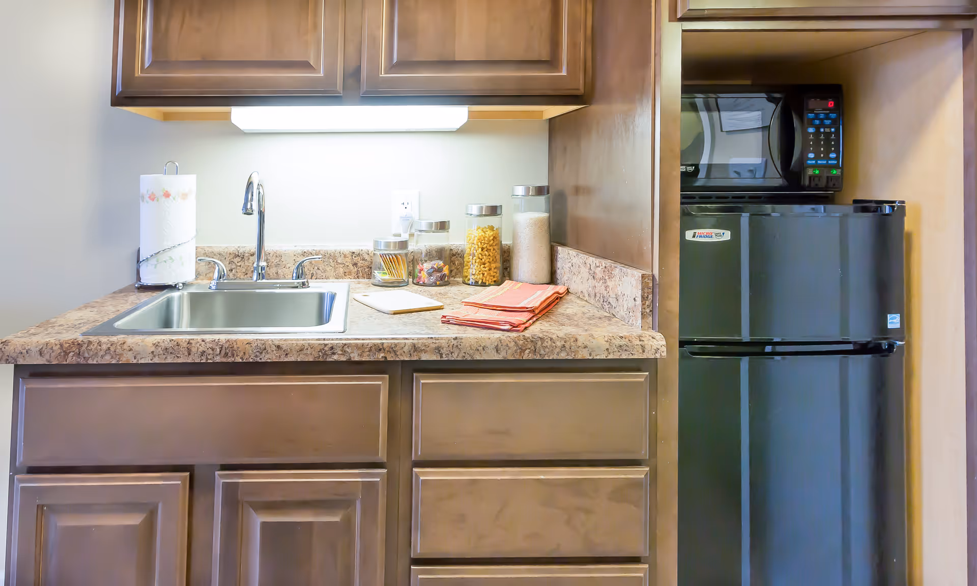 Small kitchenette with a sink, countertop, cabinets, microwave, and compact refrigerator.