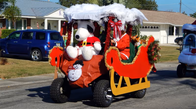A golf cart decorated as a red Santa sleigh with a large Snoopy plush and holiday decorations driving down a residential street.