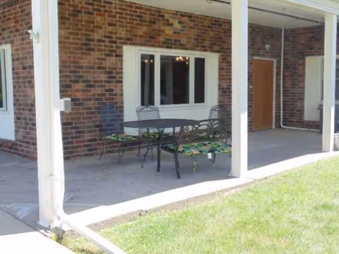 Brick building patio with a metal table and chairs under a covered porch.