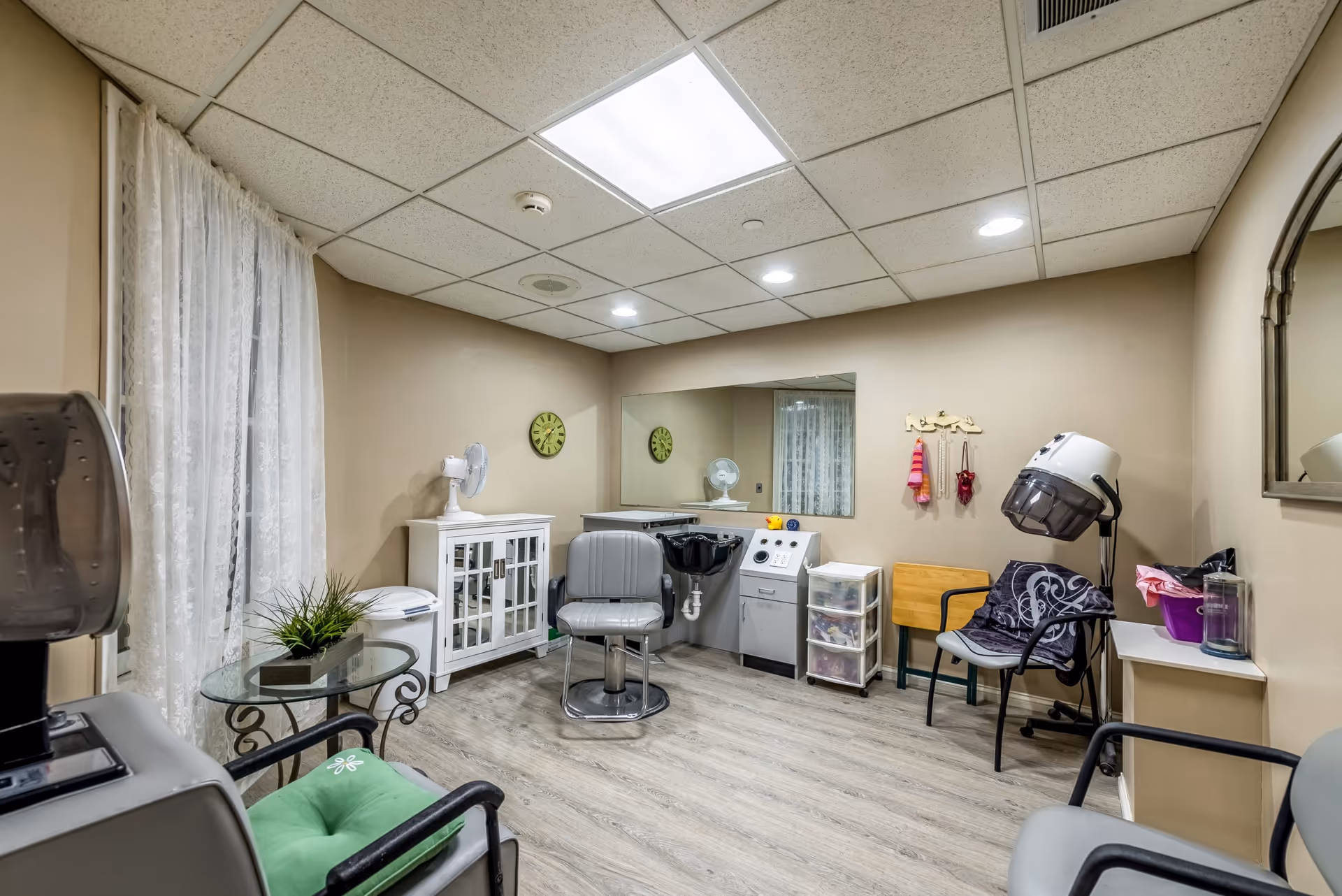 Small salon-style room with hairdressing chairs, a hooded dryer, sink station, and seating.