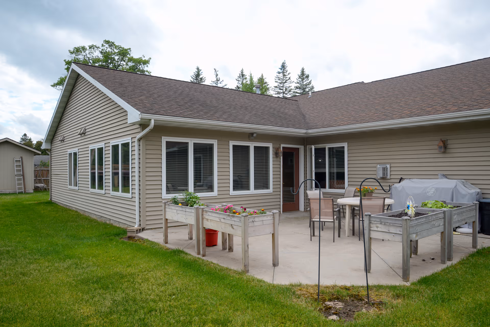 Back patio of a single-story senior living building with raised planters, patio furniture, and a grassy yard.